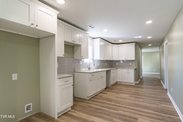 kitchen featuring sink, white cabinets, light hardwood / wood-style flooring, and tasteful backsplash