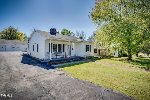 view of front of home with a porch, a front yard, an outbuilding, and a garage