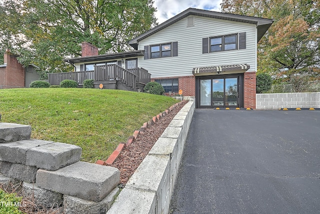 tri-level home with fence, a front lawn, brick siding, and a deck
