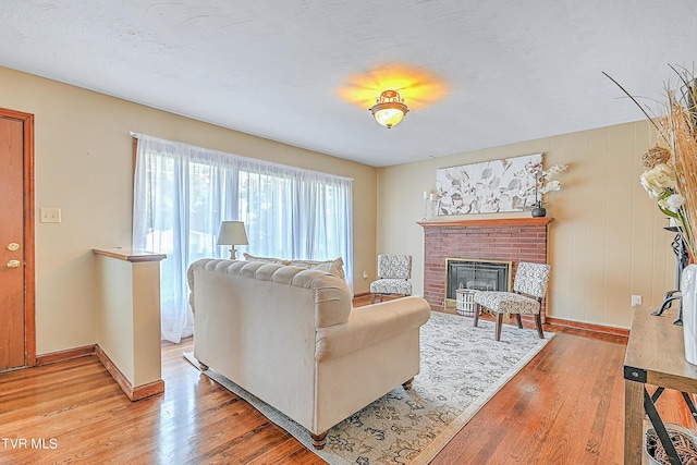 living room featuring baseboards, a brick fireplace, and light wood finished floors
