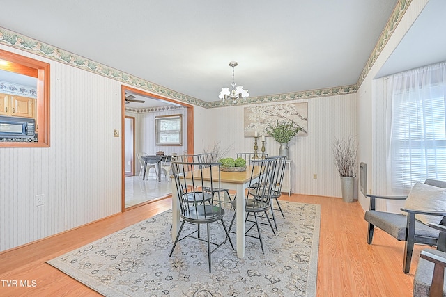 dining area with wallpapered walls, wood finished floors, and an inviting chandelier