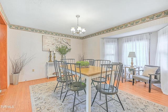 dining area featuring light wood finished floors, wallpapered walls, baseboards, and a notable chandelier