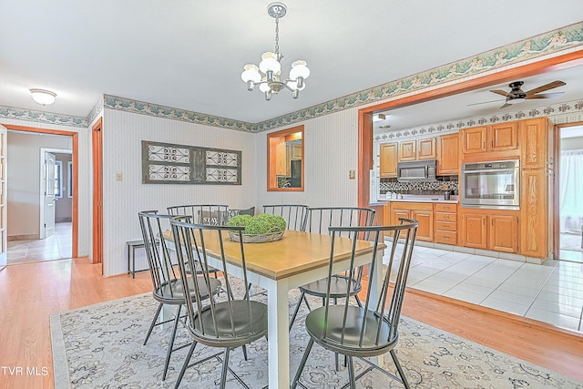 dining space with wallpapered walls, light wood finished floors, and ceiling fan with notable chandelier