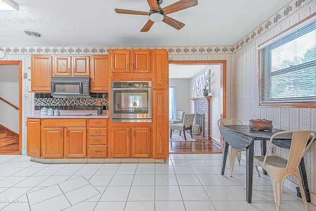 kitchen with wallpapered walls, black microwave, oven, ceiling fan, and light countertops