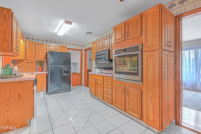 kitchen with a sink, light tile patterned flooring, backsplash, light countertops, and black appliances