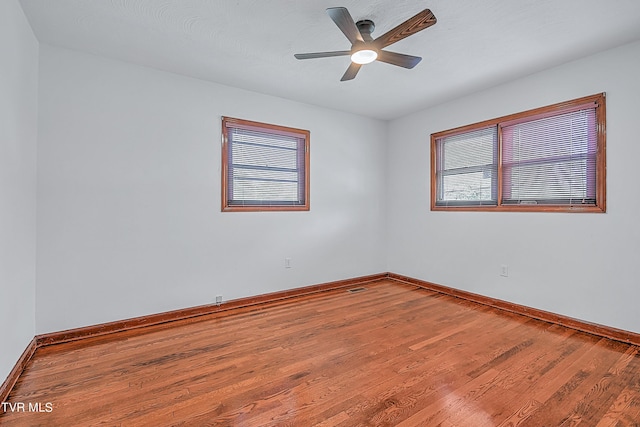 spare room featuring wood finished floors, visible vents, a ceiling fan, and baseboards