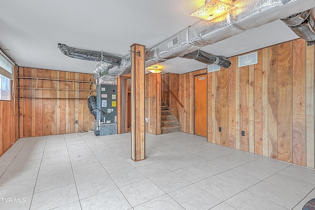 basement with visible vents, heating unit, wood walls, and stairway
