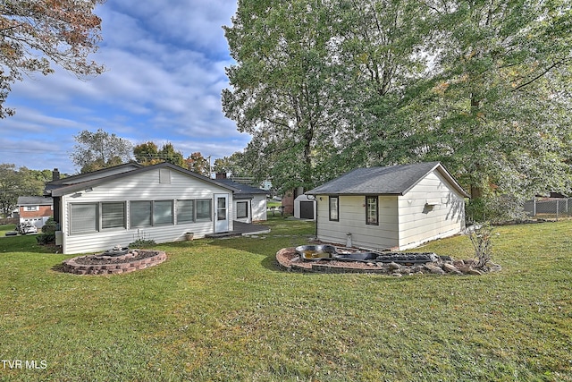 back of property featuring a fire pit, a yard, and an outbuilding