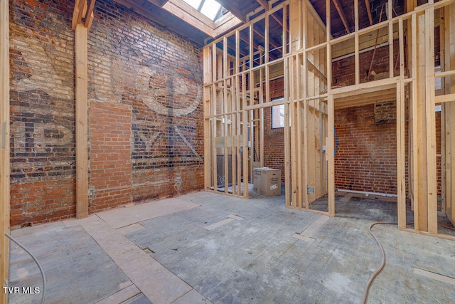 miscellaneous room featuring a skylight, a towering ceiling, and brick wall