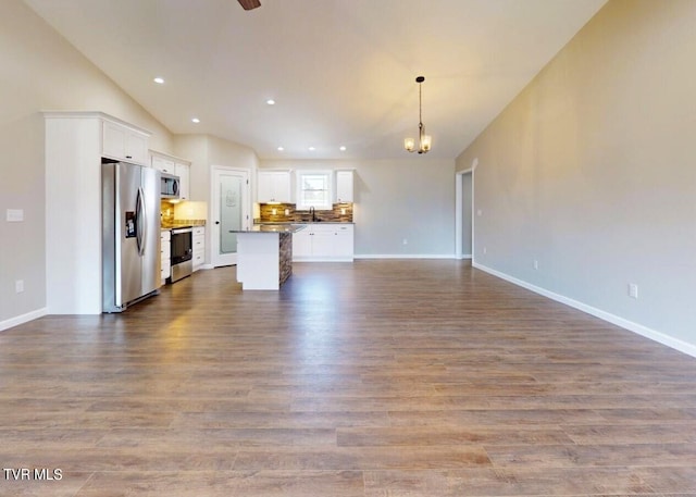 unfurnished living room with sink, hardwood / wood-style floors, vaulted ceiling, and a notable chandelier