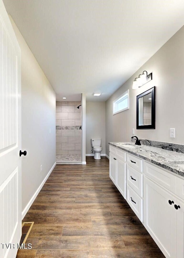 bathroom featuring vanity, a tile shower, hardwood / wood-style flooring, and toilet