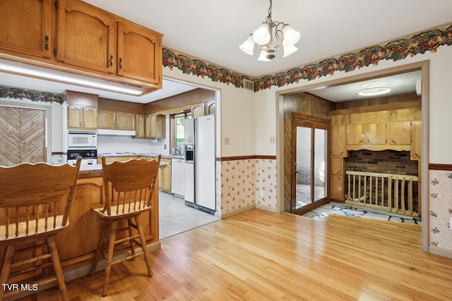 kitchen with white appliances, light wood-type flooring, decorative light fixtures, a notable chandelier, and a breakfast bar