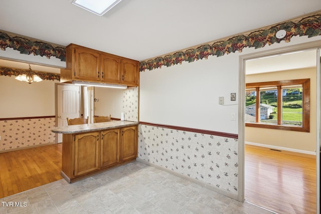 kitchen with an inviting chandelier, light stone counters, light wood-type flooring, and kitchen peninsula