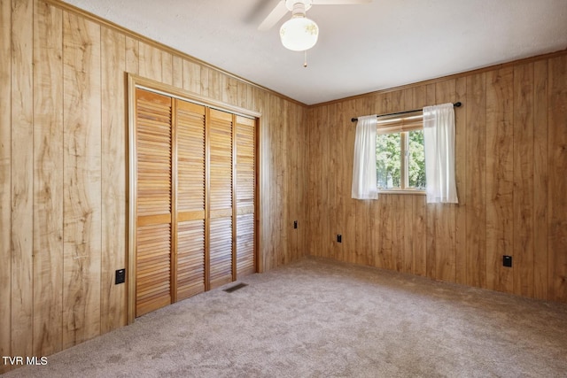 unfurnished bedroom with a closet, ceiling fan, carpet, and wooden walls