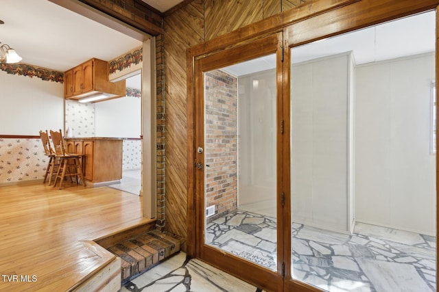 entryway with brick wall, light wood-type flooring, indoor bar, and wood walls