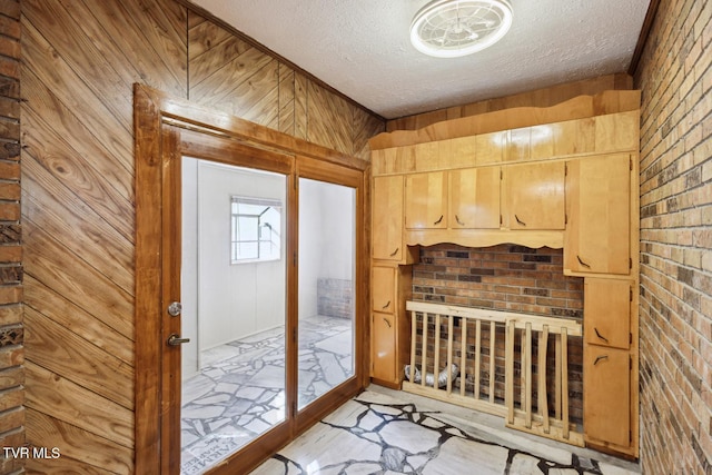 doorway to outside featuring brick wall, a textured ceiling, and wood walls