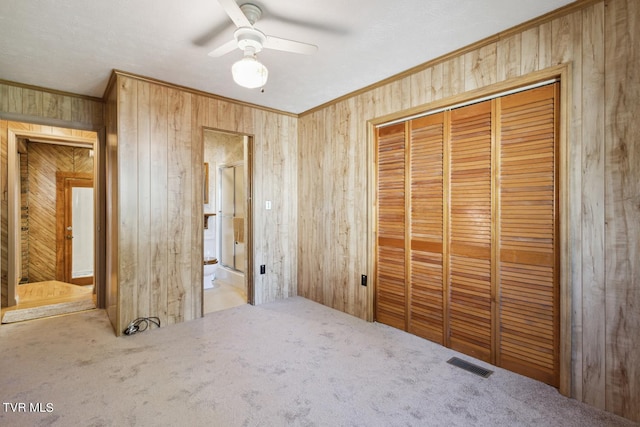 unfurnished bedroom with a closet, wood walls, light colored carpet, and ceiling fan