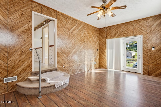 empty room featuring hardwood / wood-style floors, ceiling fan, a textured ceiling, and wood walls