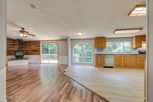 kitchen with a wood stove, light hardwood / wood-style flooring, stainless steel dishwasher, wood walls, and decorative backsplash