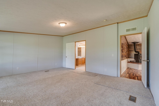 unfurnished bedroom featuring ensuite bathroom, a wood stove, a textured ceiling, and carpet floors