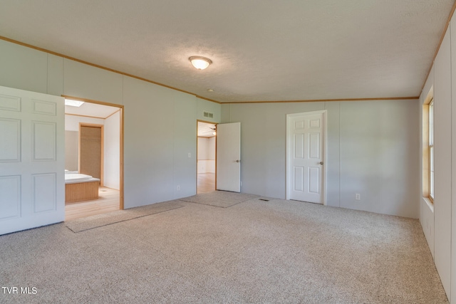 unfurnished bedroom with a textured ceiling, light colored carpet, ensuite bath, and ornamental molding