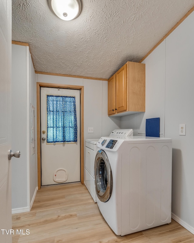 clothes washing area with cabinets, light hardwood / wood-style flooring, a textured ceiling, washer and clothes dryer, and ornamental molding