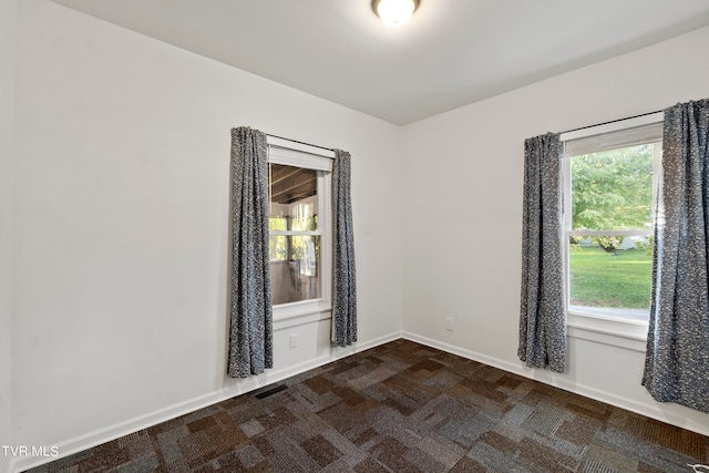 empty room featuring plenty of natural light and dark colored carpet