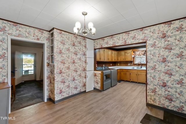 kitchen with sink, light hardwood / wood-style flooring, hanging light fixtures, and washing machine and clothes dryer