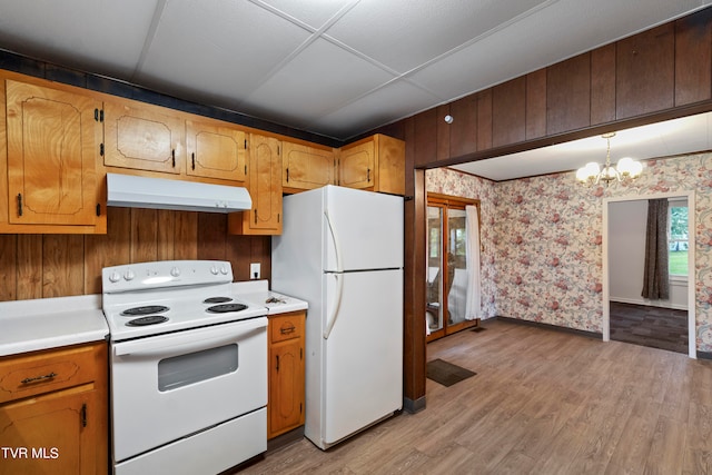 kitchen with white appliances, wood walls, light wood-type flooring, hanging light fixtures, and a notable chandelier