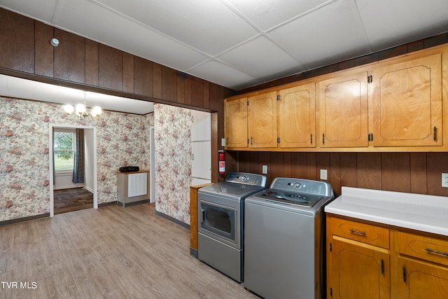 laundry room featuring cabinets, washing machine and dryer, wooden walls, and light wood-type flooring