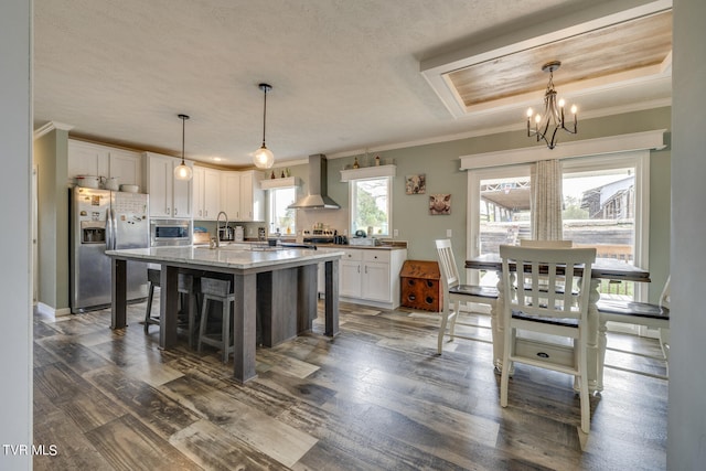 kitchen with wall chimney range hood, white cabinets, stainless steel appliances, and a wealth of natural light