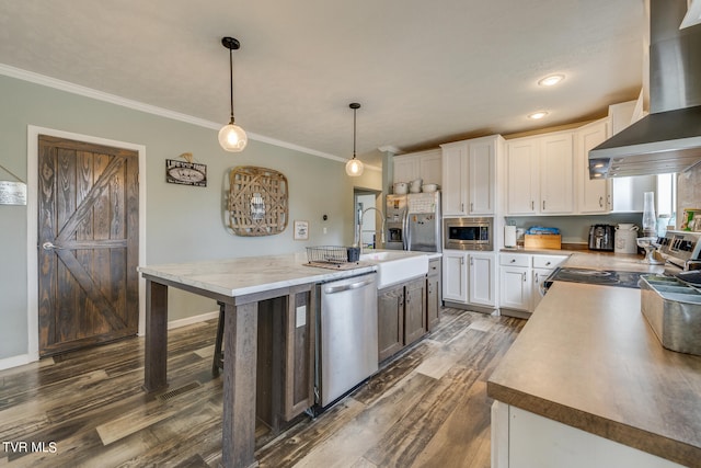 kitchen featuring a kitchen island with sink, ornamental molding, pendant lighting, wall chimney exhaust hood, and stainless steel appliances