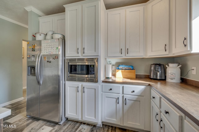 kitchen with stainless steel appliances, ornamental molding, light hardwood / wood-style flooring, and white cabinets