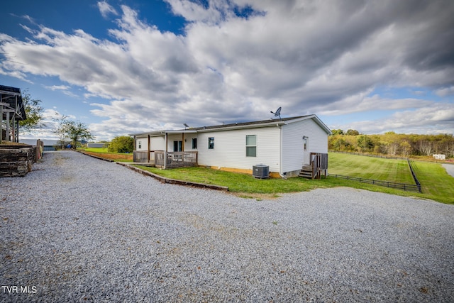 rear view of property featuring central air condition unit and a lawn