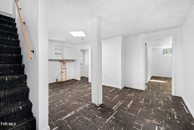 basement with a paneled ceiling and dark colored carpet