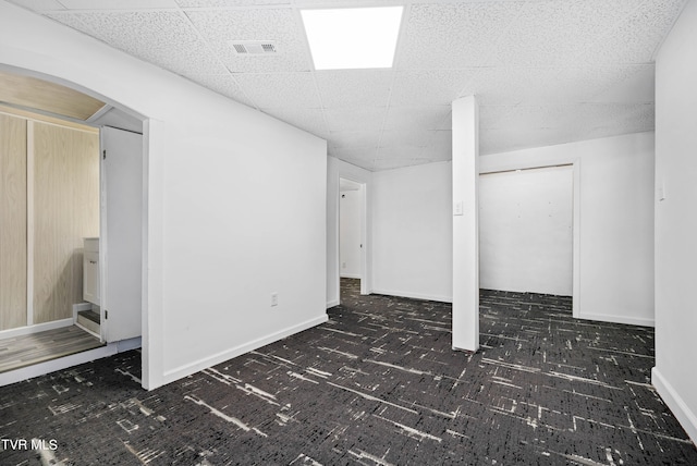 basement featuring a paneled ceiling and dark carpet