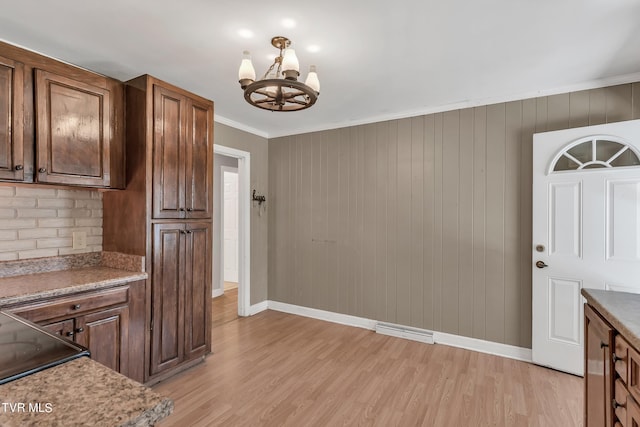 kitchen with a notable chandelier, ornamental molding, wood walls, and light wood-type flooring