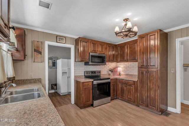 kitchen featuring appliances with stainless steel finishes, sink, light wood-type flooring, crown molding, and an inviting chandelier