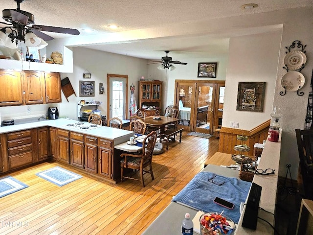 kitchen with kitchen peninsula, a textured ceiling, light wood-type flooring, and ceiling fan