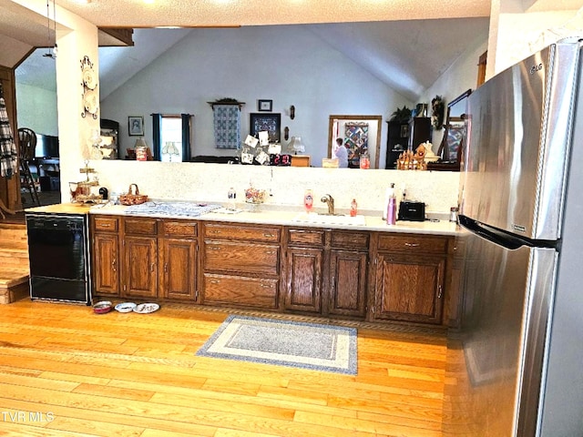 kitchen featuring lofted ceiling, light hardwood / wood-style flooring, sink, a textured ceiling, and stainless steel refrigerator