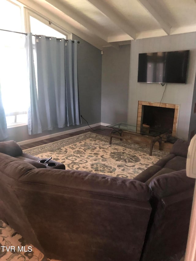 living room with a tiled fireplace and vaulted ceiling with beams