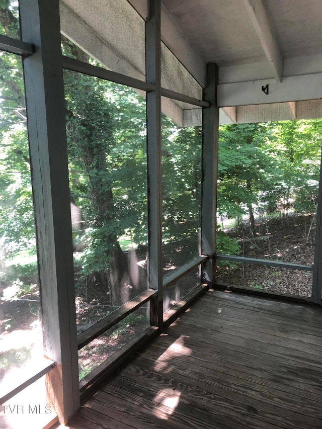 unfurnished sunroom featuring beam ceiling and plenty of natural light