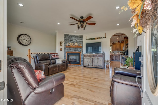 living room featuring light hardwood / wood-style floors, crown molding, a stone fireplace, and ceiling fan