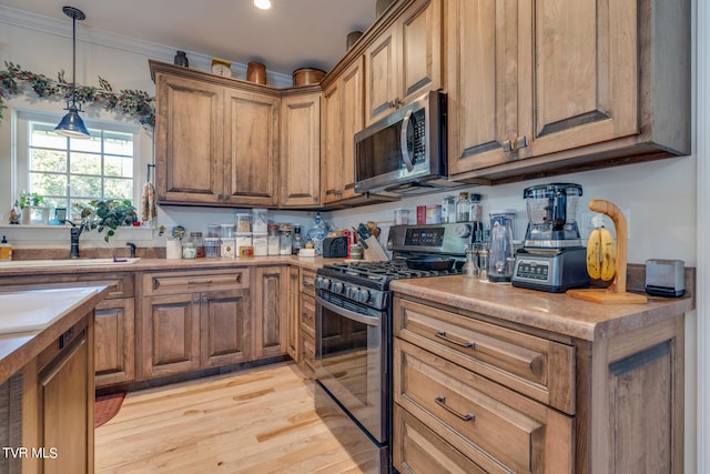 kitchen featuring ornamental molding, hanging light fixtures, stainless steel appliances, and light hardwood / wood-style floors