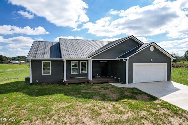 view of front of home with a front yard, an attached garage, covered porch, concrete driveway, and metal roof