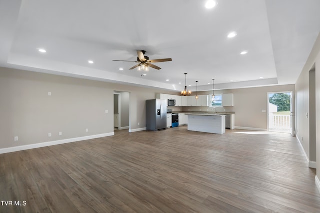 unfurnished living room featuring a tray ceiling, ceiling fan, sink, and light hardwood / wood-style floors