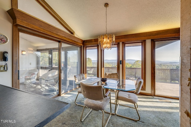 carpeted dining room with a mountain view, a notable chandelier, a textured ceiling, and vaulted ceiling