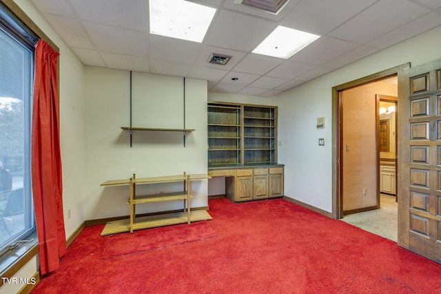 interior space featuring built in desk, a drop ceiling, and light carpet