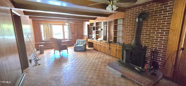 living room with beam ceiling, ceiling fan, a wood stove, and wood walls