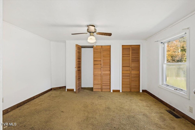 unfurnished bedroom with multiple closets, carpet flooring, and ceiling fan